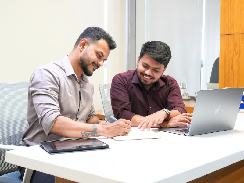 Two iConsultera staff in Ahmedabad office collaborating and signing documents with laptop